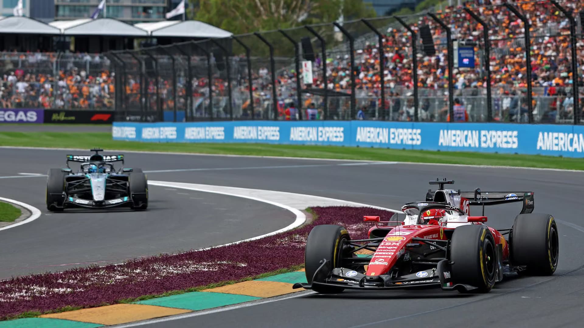 A red Formula 1 car leads a silver car through a corner at Albert Park with full grandstands behind them