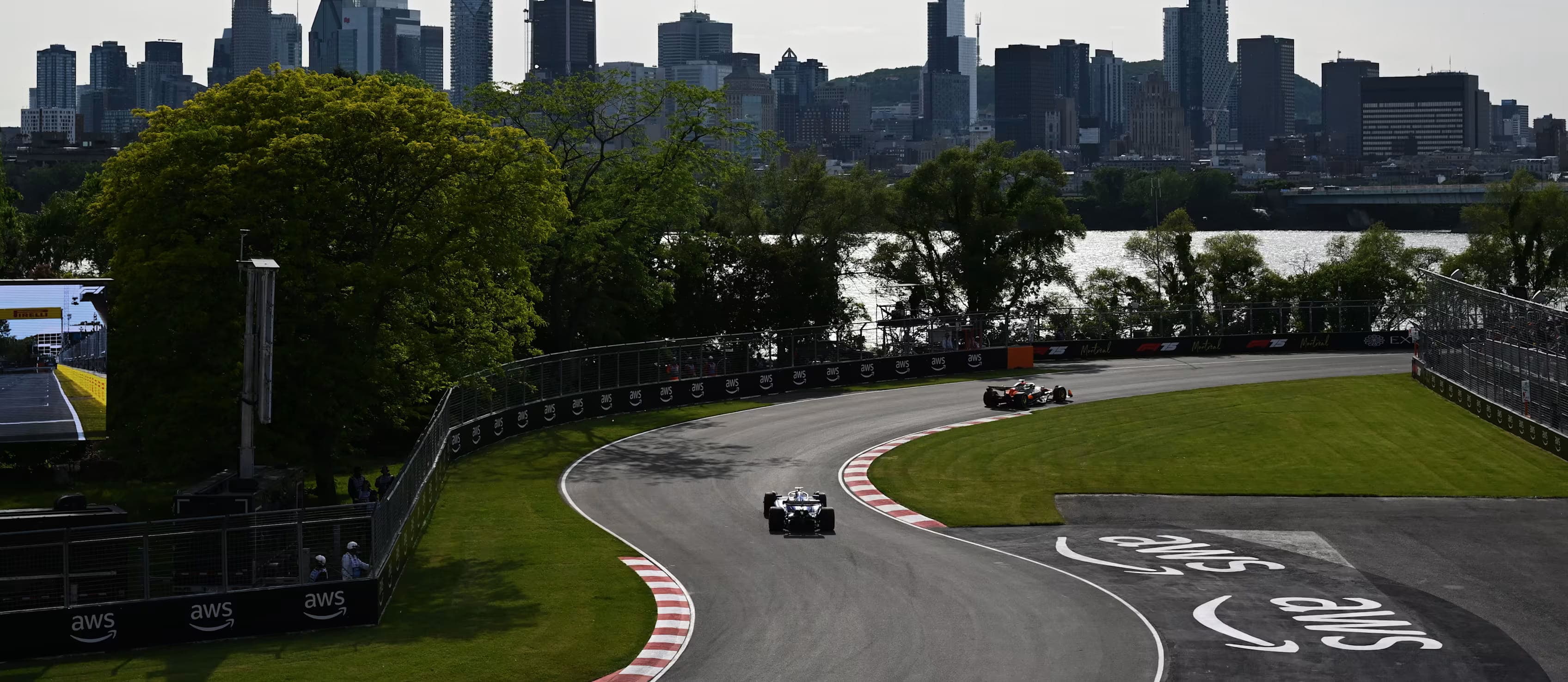 Formula 1 cars race through Circuit Gilles Villeneuve with the Montreal skyline rising beyond the trees