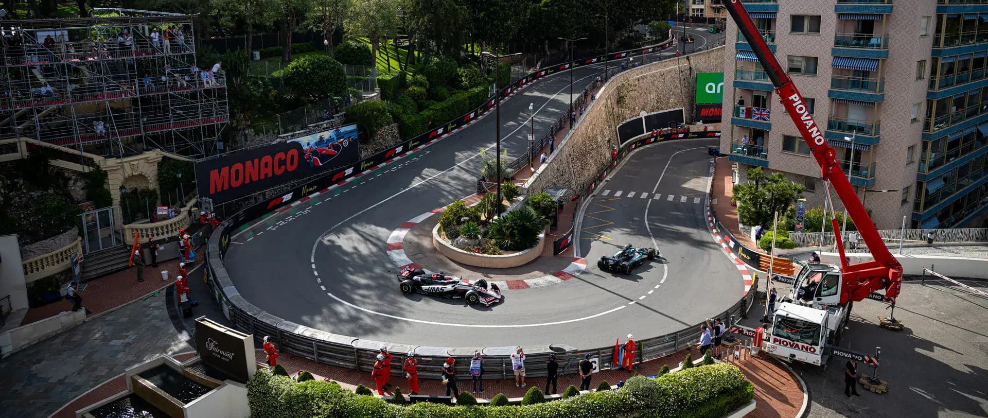 Two Formula 1 cars negotiate Monaco's Grand Hotel Hairpin between buildings and packed grandstands